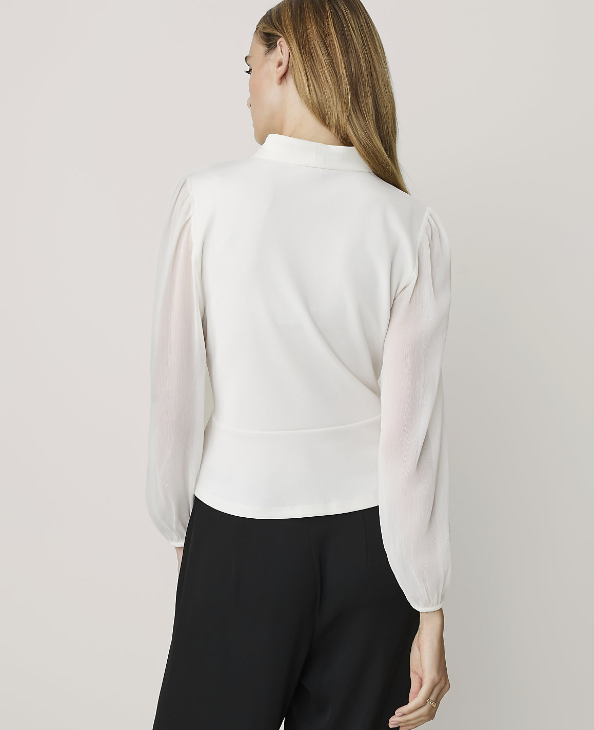 A woman in a white blouse and black pants stands against a plain white background.