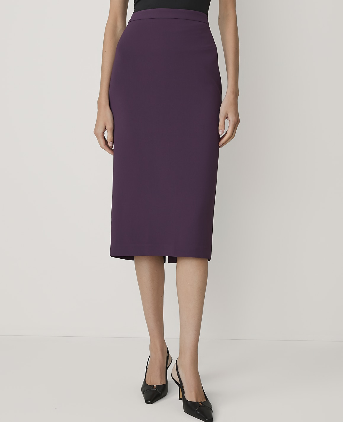 A woman in a purple pencil skirt and black heels stands against a plain white background.