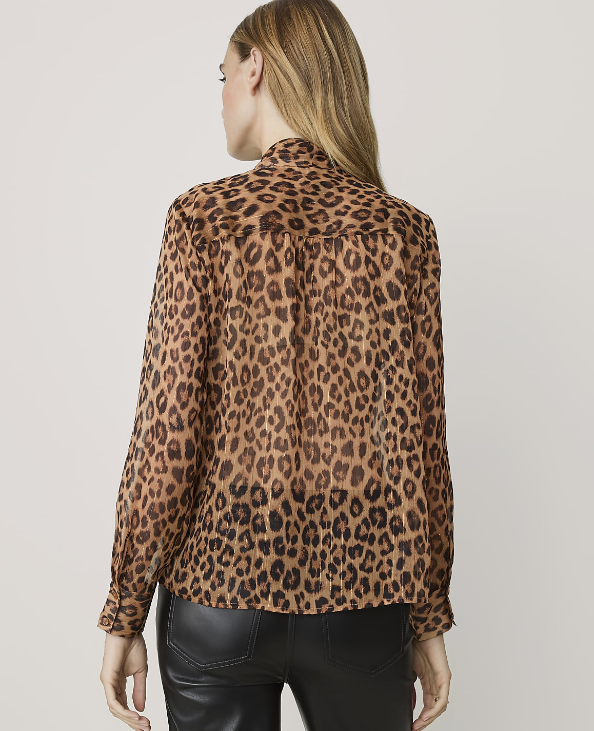 A woman in a leopard print blouse stands against a plain, light-colored background.