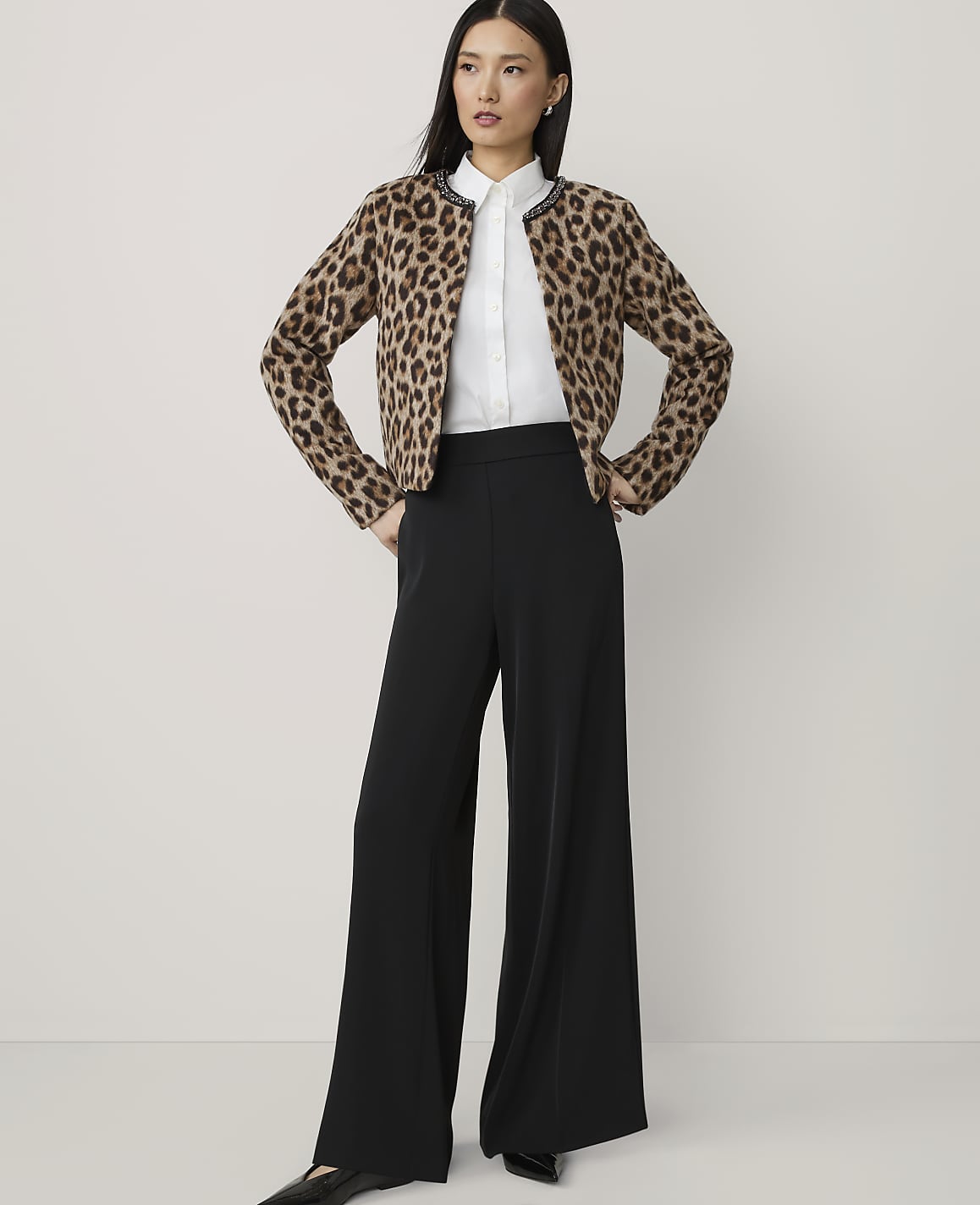 A woman in a leopard print cardigan and black wide-leg pants stands against a plain, light gray background.
