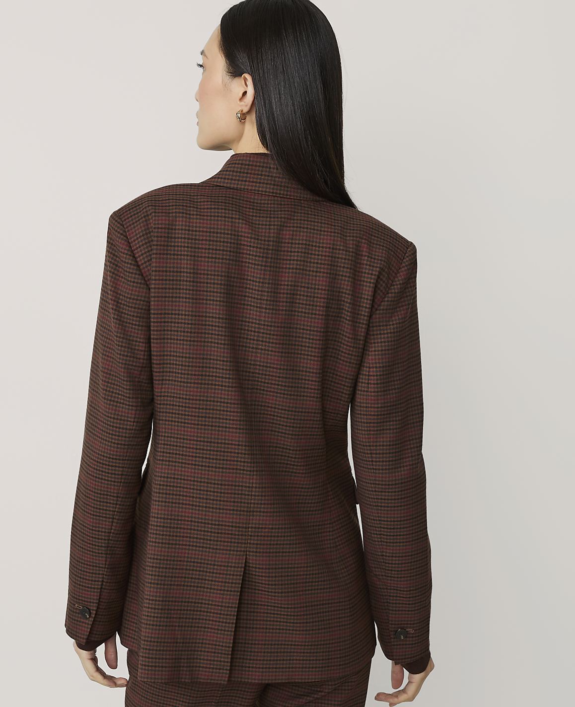 A woman in a brown plaid blazer stands against a plain white background.