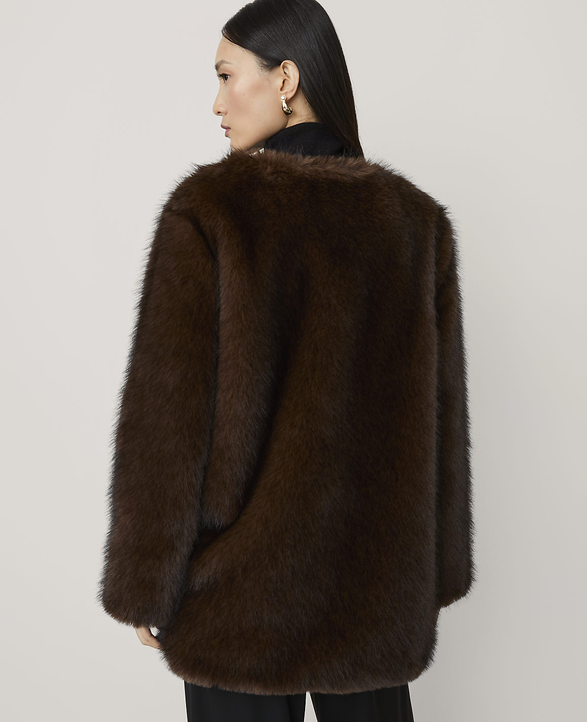 A woman in a brown faux fur coat stands against a plain white background.