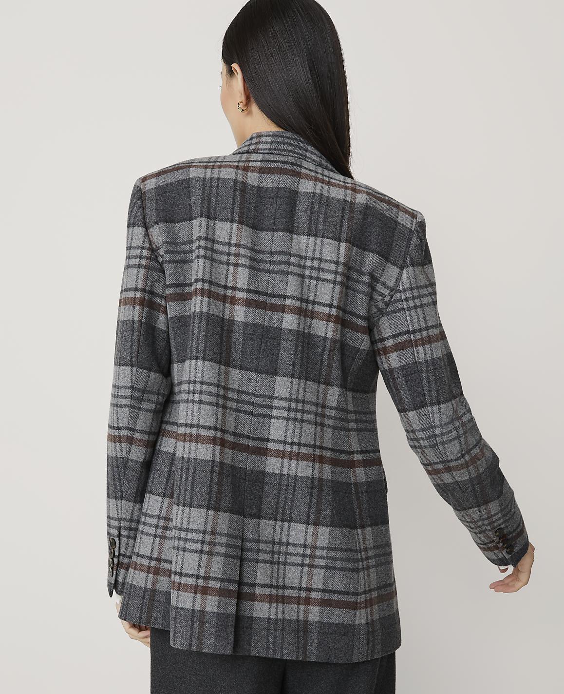 A woman in a gray plaid blazer stands against a plain, light gray background.