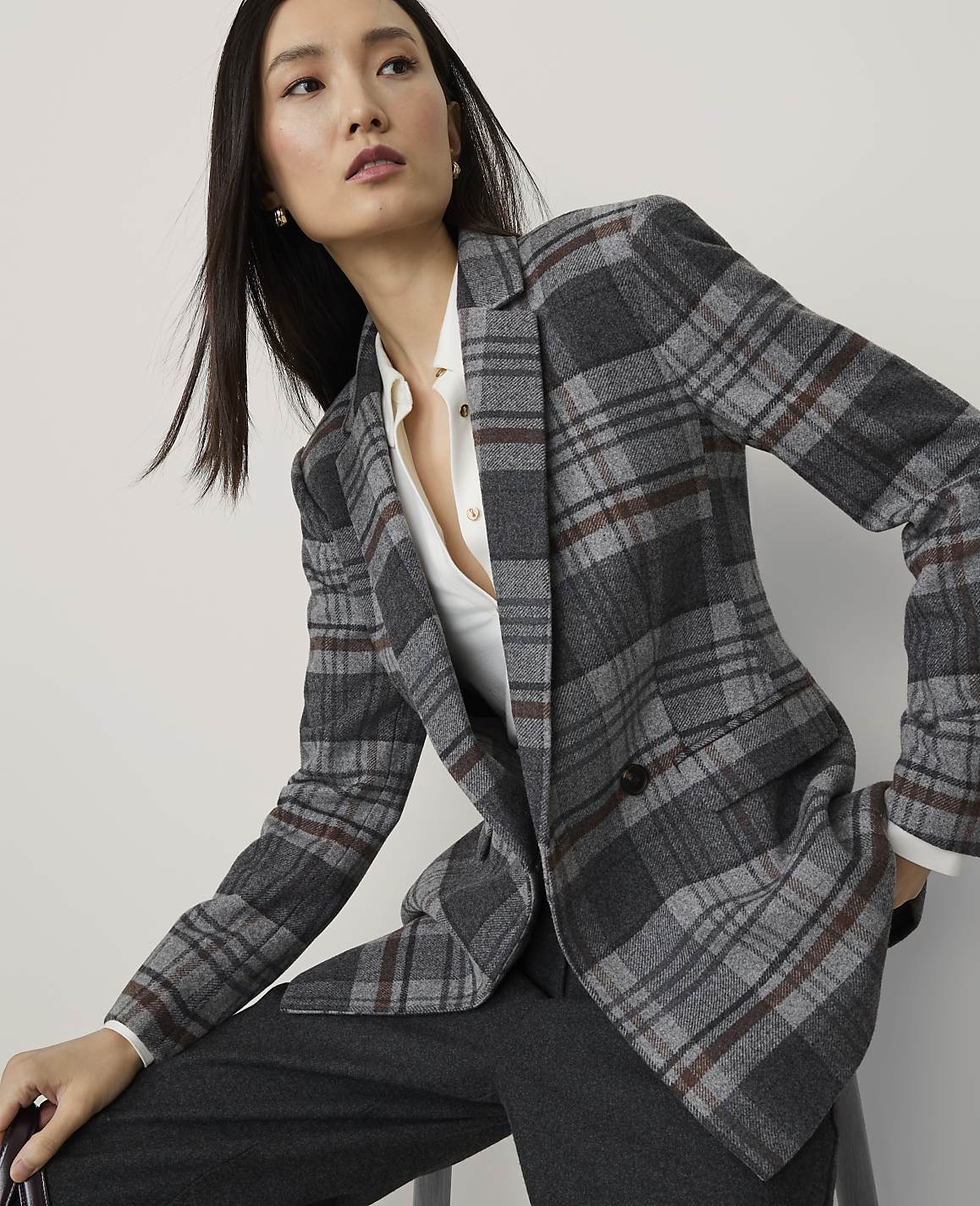 A woman in a plaid blazer and dark pants poses against a plain, light gray background.