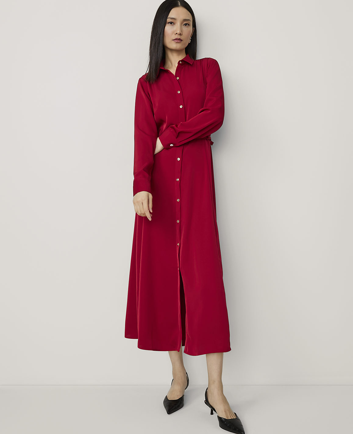 A woman in a red dress stands with her arms crossed against a plain white background.