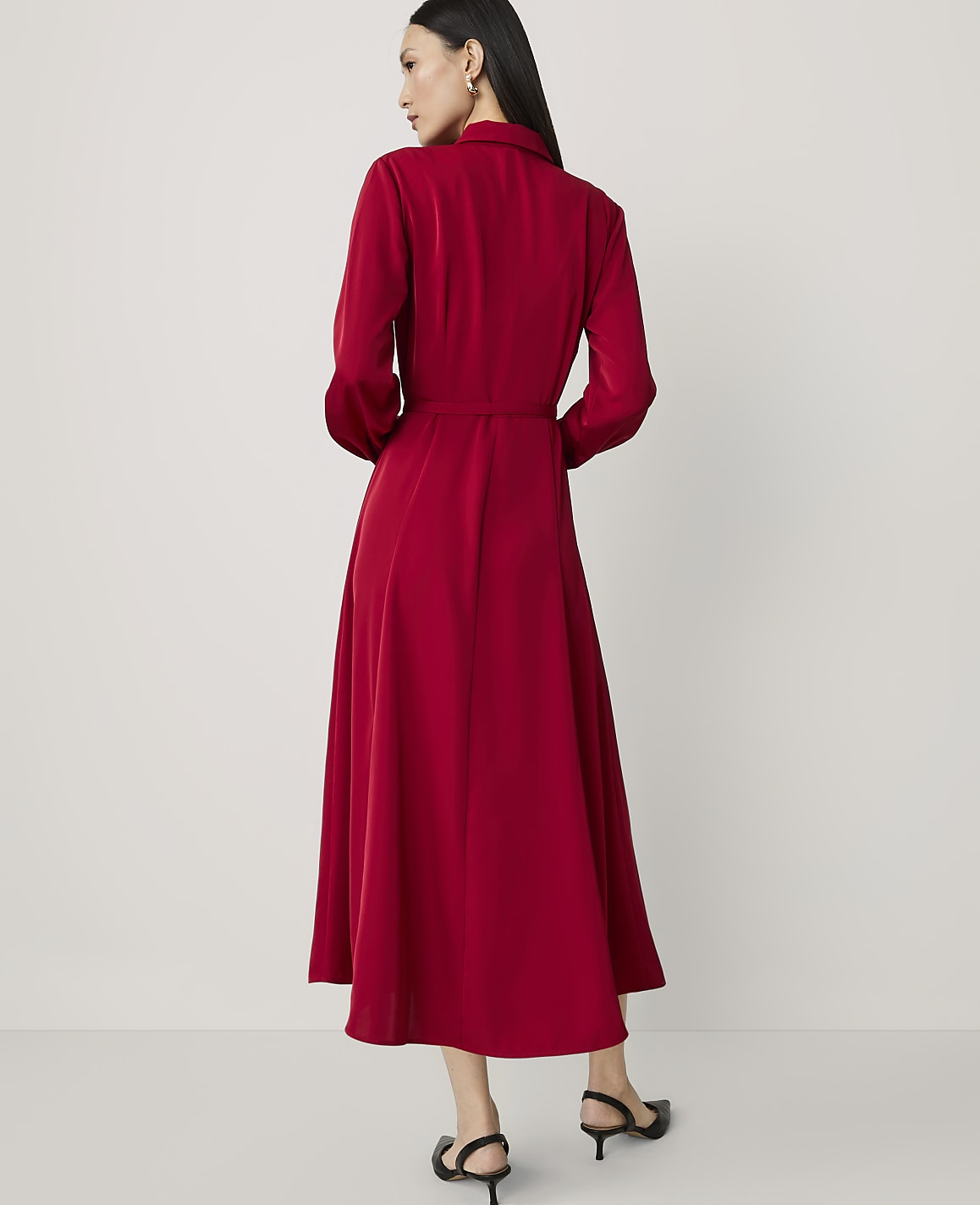 A woman in a red dress stands against a plain white background.