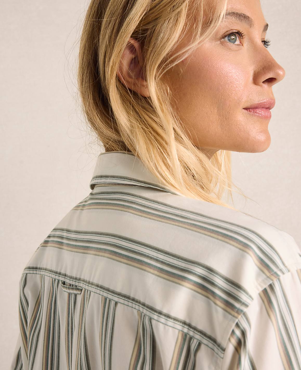 A woman with blonde hair, wearing a striped shirt, is shown in profile against a plain background.