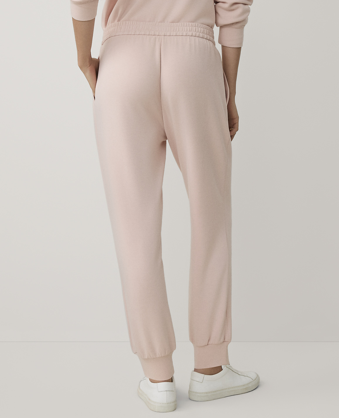 A person wearing light pink sweatpants and white sneakers stands against a plain white background.