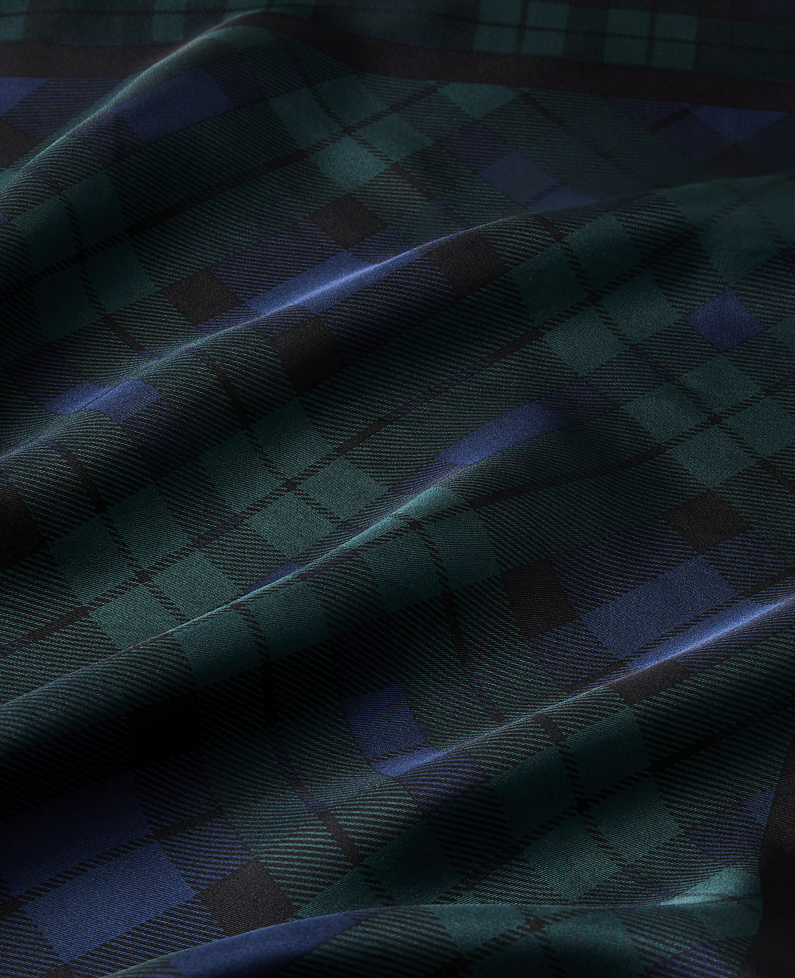 Draped folds of dark green and blue plaid fabric create a textured landscape of light and shadow.
