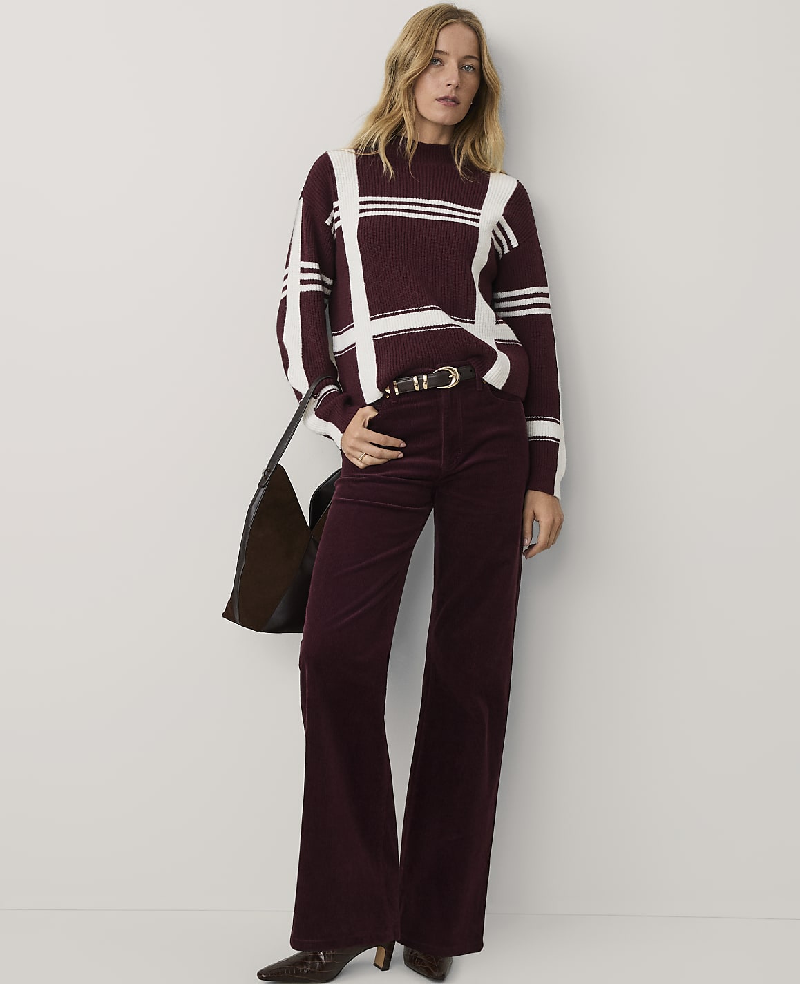 A woman wearing a burgundy and white striped sweater and matching flared trousers stands against a plain white background.
