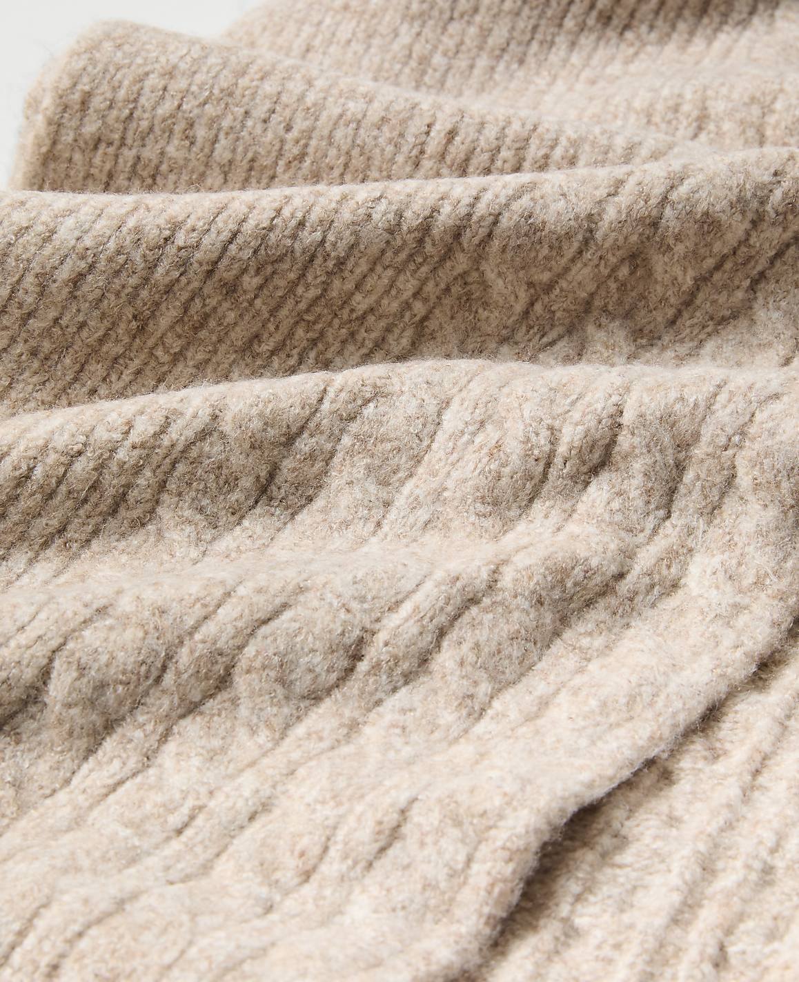 Close-up of textured, beige ribbed fabric folding in the foreground against a soft, blurred background of the same material.