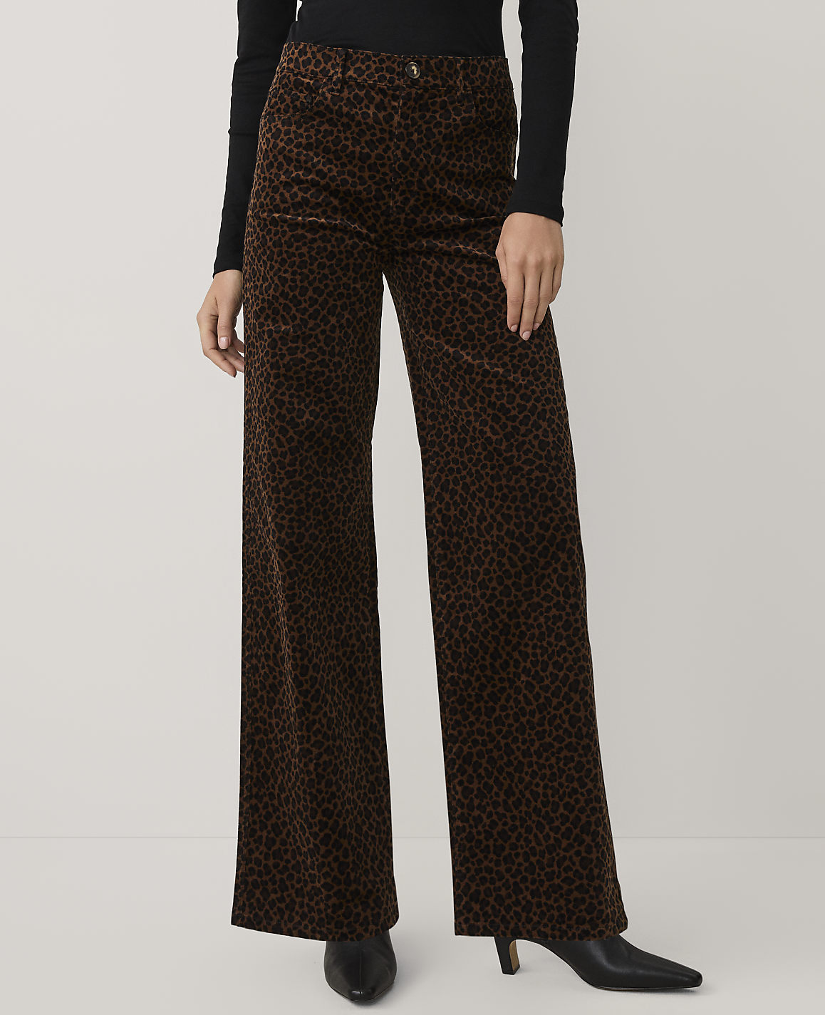A person wearing a black top and brown leopard-print wide-leg trousers stands against a plain light gray background.