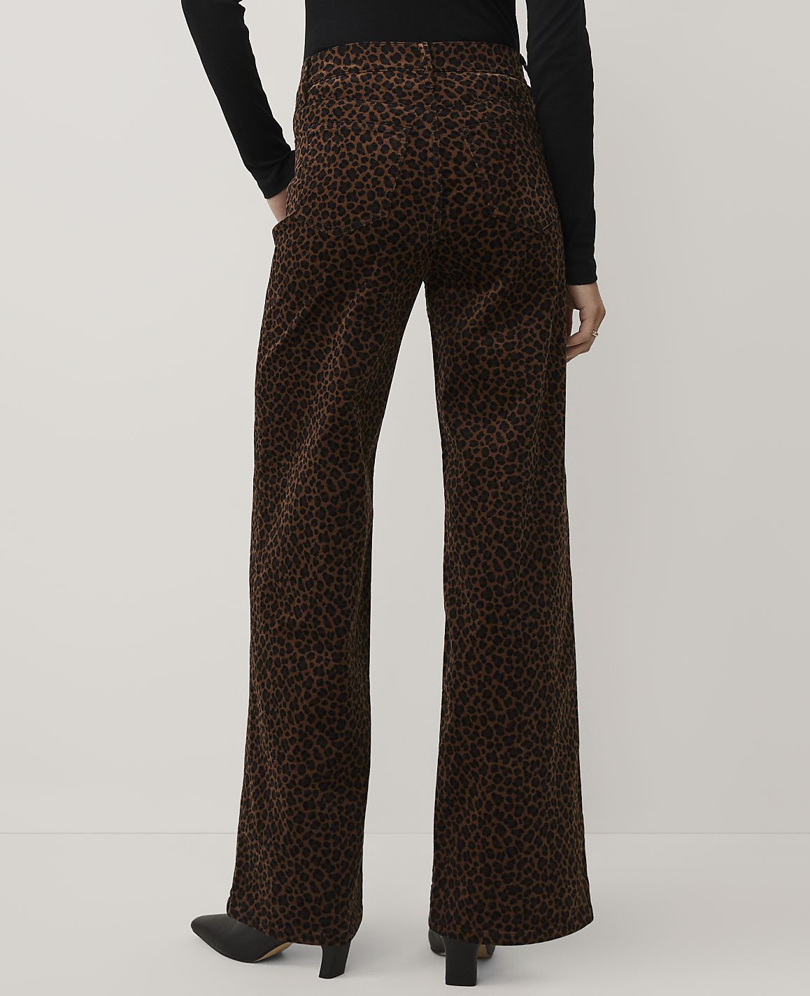 A person wearing a black top and brown leopard-print wide-leg trousers stands against a plain light gray background.