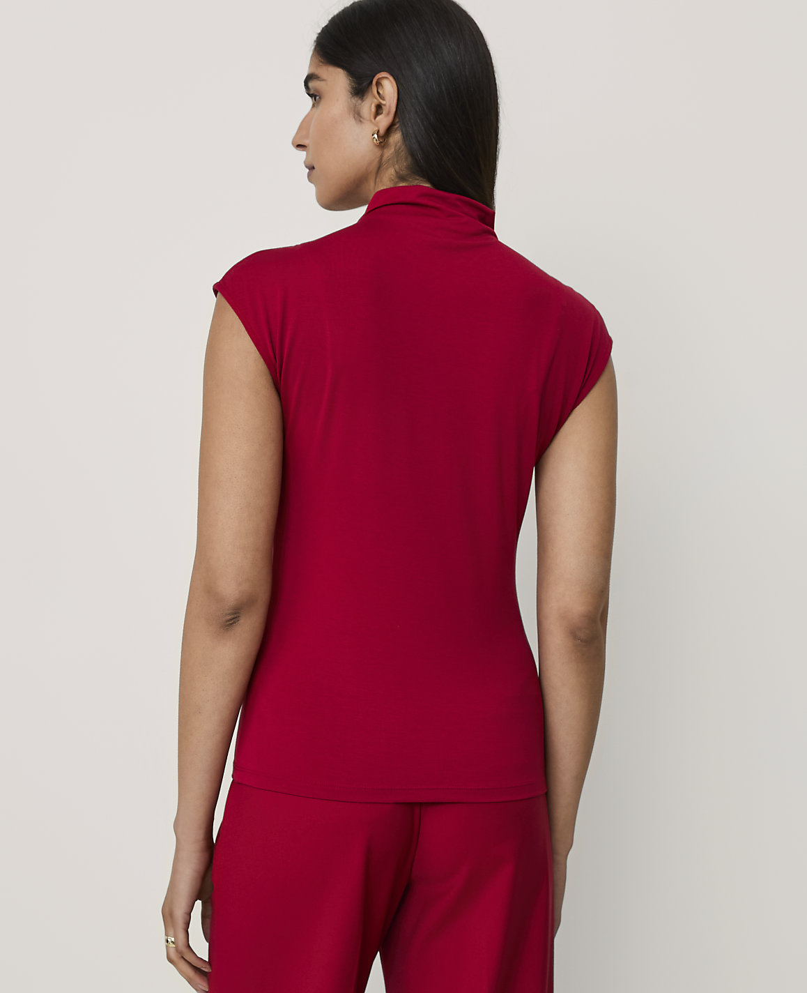 A woman wearing a red short-sleeved top and matching pants stands with her back to the camera against a plain light gray background.