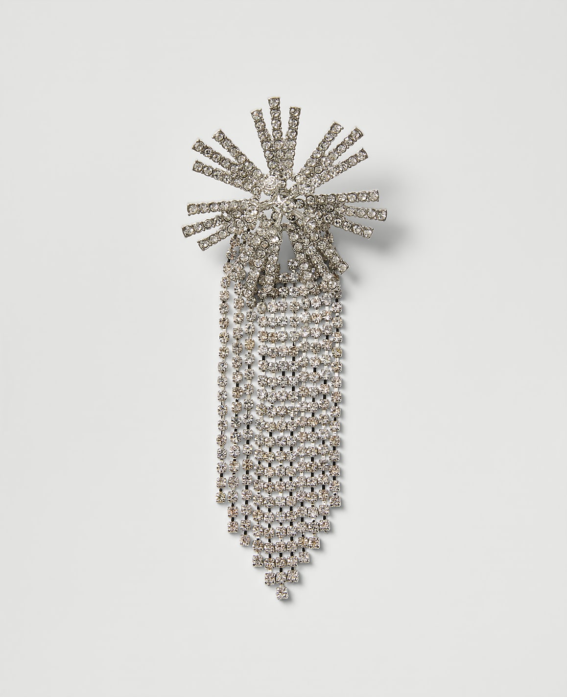 A sparkling rhinestone brooch with a sunburst top and cascading fringe is centered against a plain, light gray background.