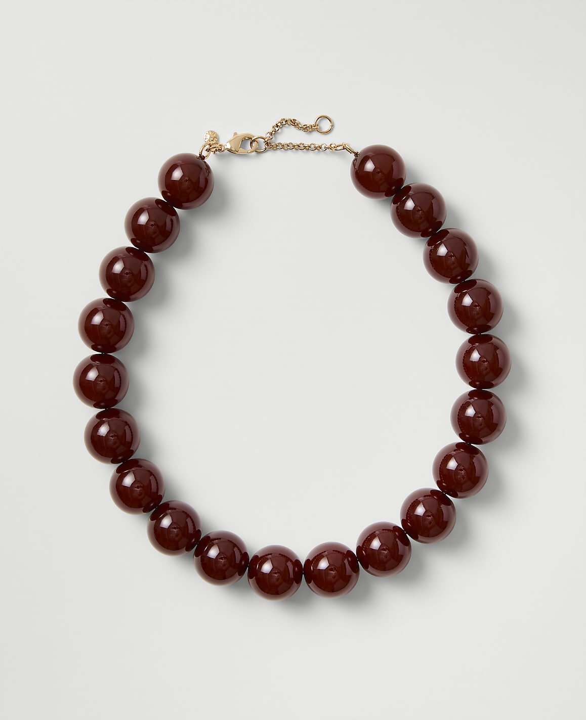 A necklace of polished deep red beads with a gold clasp rests on a plain light gray background.