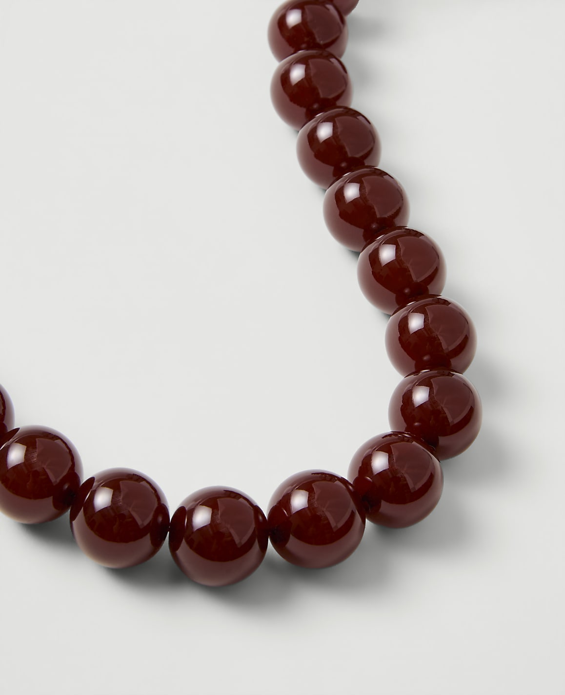 A string of glossy, deep red beads curves across a plain white background.