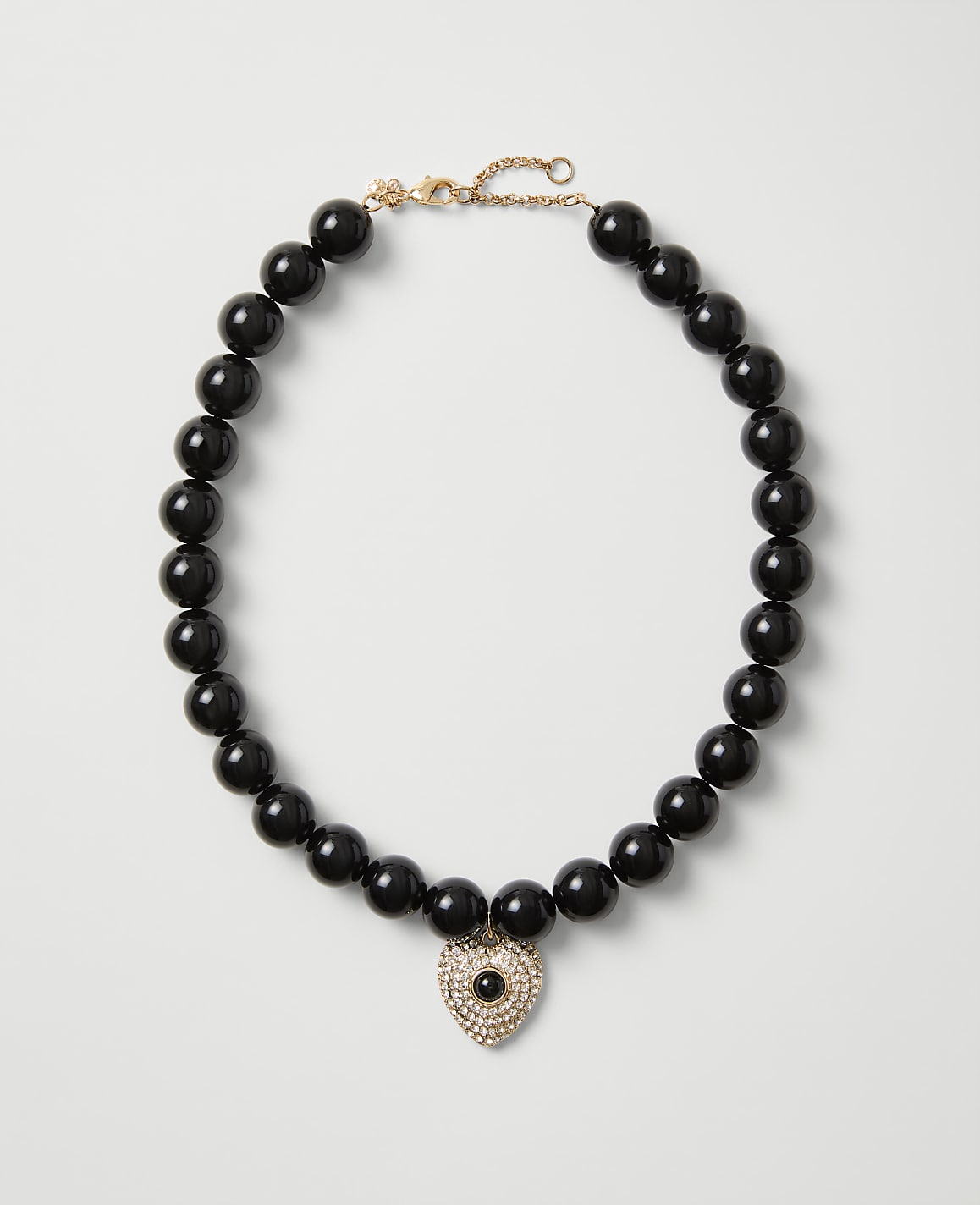 A necklace of polished black beads with a heart-shaped crystal pendant rests on a plain light gray background.