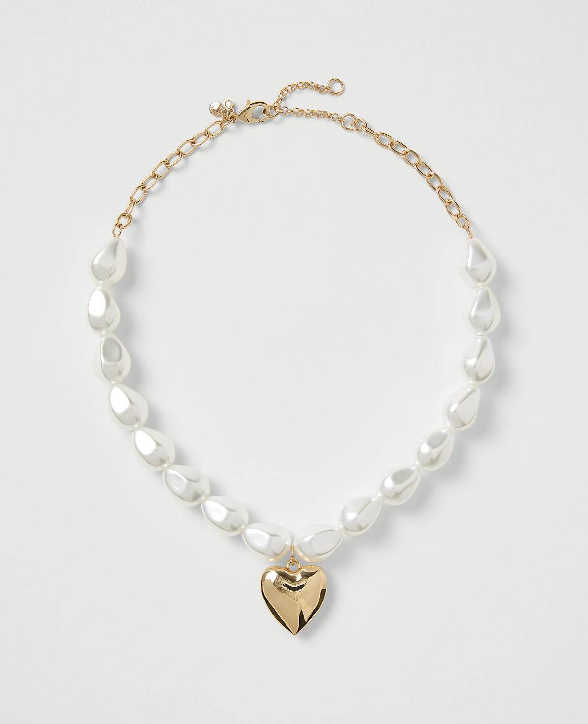 A gold-toned necklace with white teardrop pearls and a heart pendant rests on a plain white background.