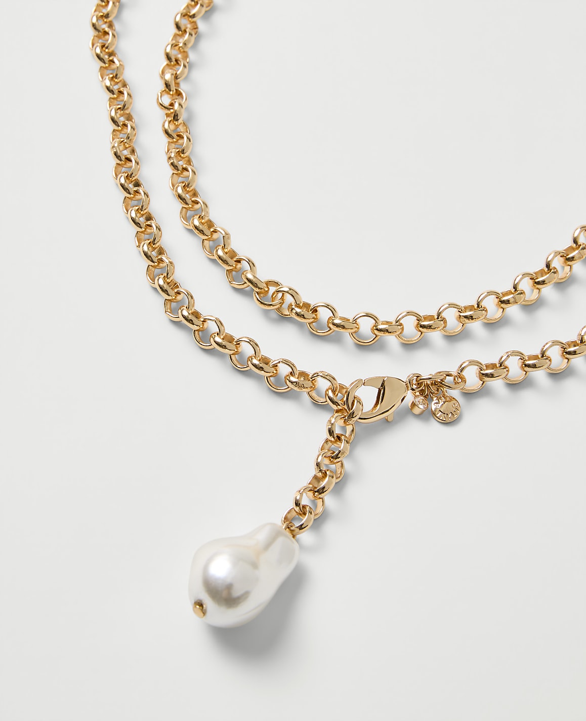 A gold chain necklace with a single white baroque pearl pendant rests against a plain light gray background.