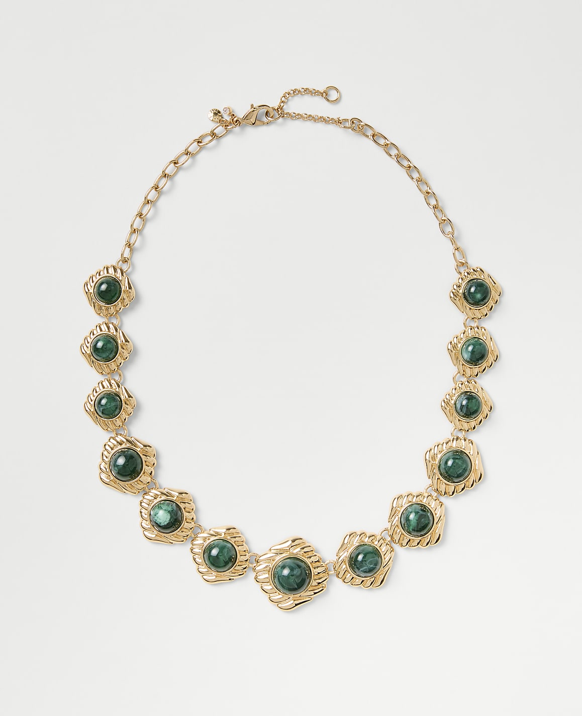 A gold chain necklace featuring green circular gemstones is centered against a plain light gray background.