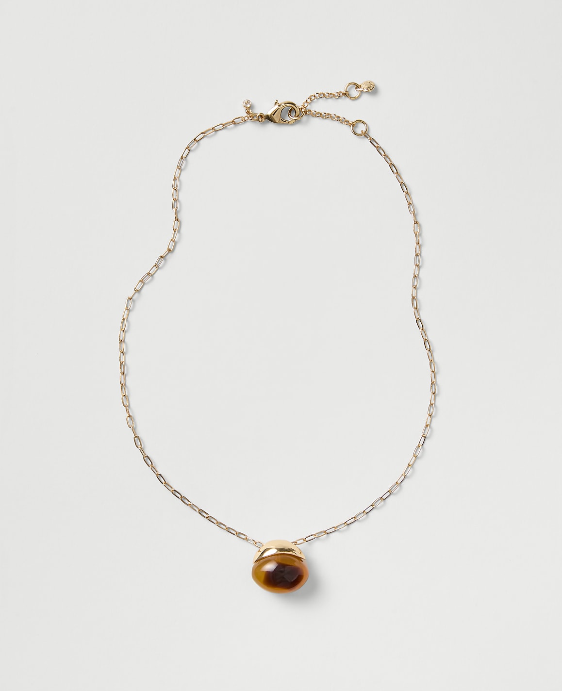 A gold chain necklace with a brown oval pendant rests on a plain light gray background.