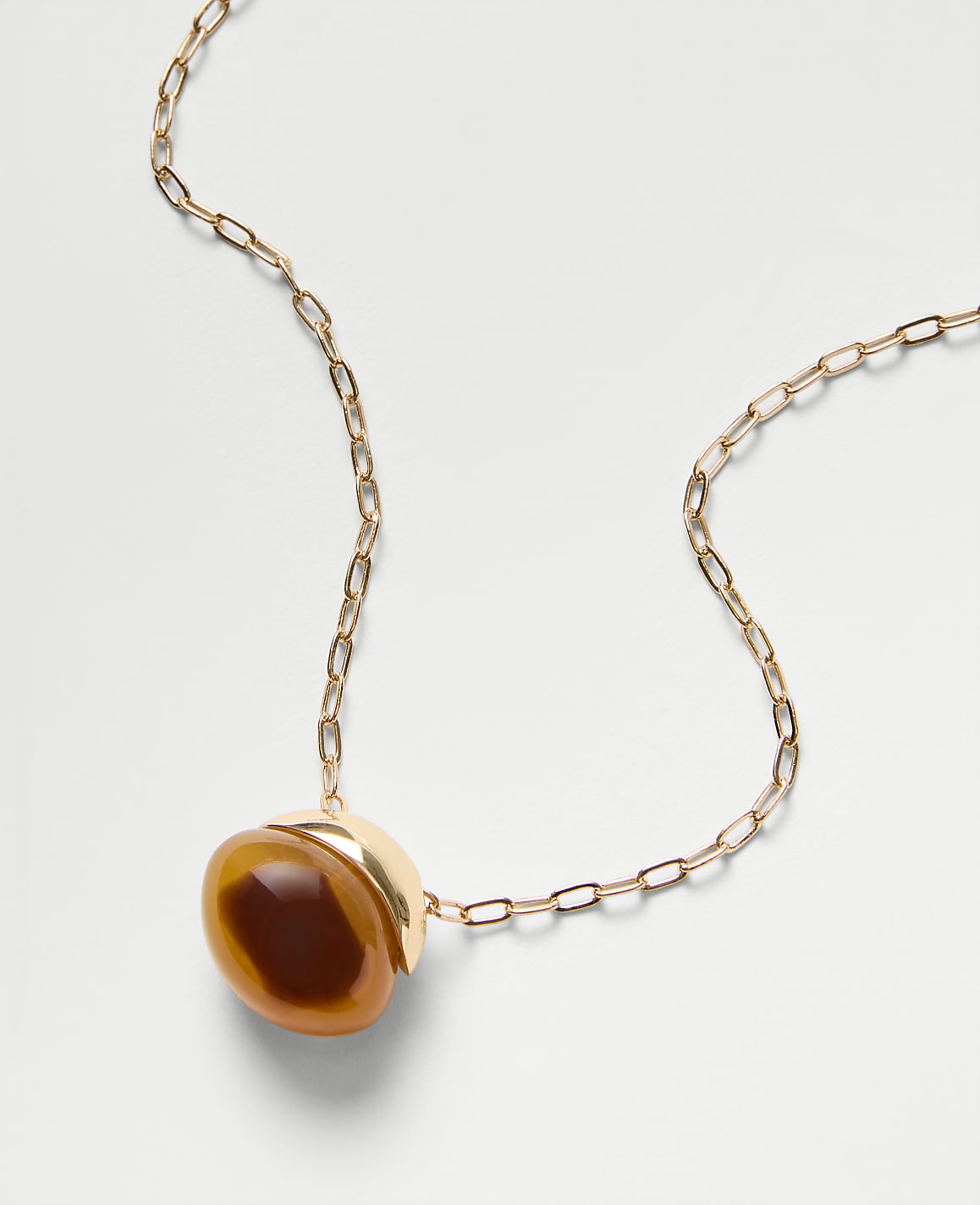 A gold chain necklace with a round, amber-colored stone pendant rests on a plain white background.