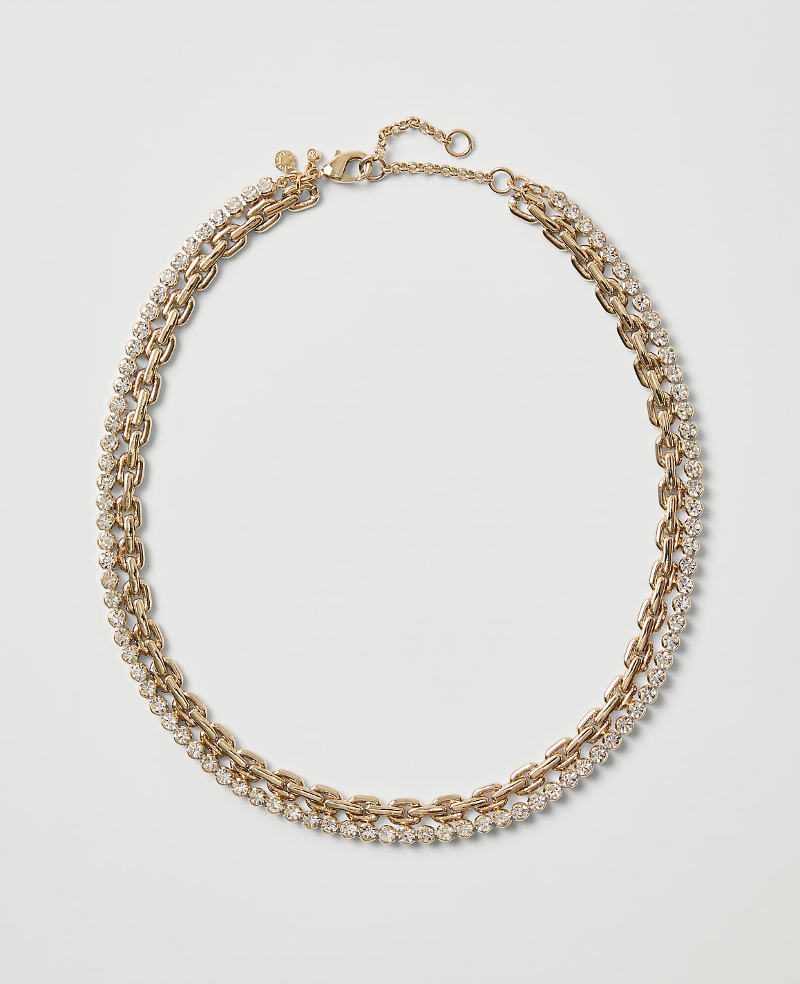 A gold-toned chain necklace embellished with sparkling crystals rests on a plain, light gray background.