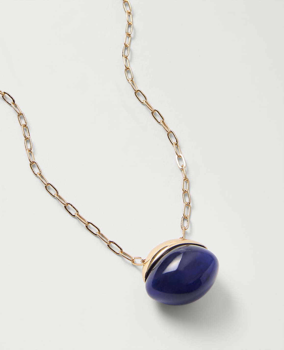 A gold chain necklace with a large, oval blue stone pendant rests on a plain white background.