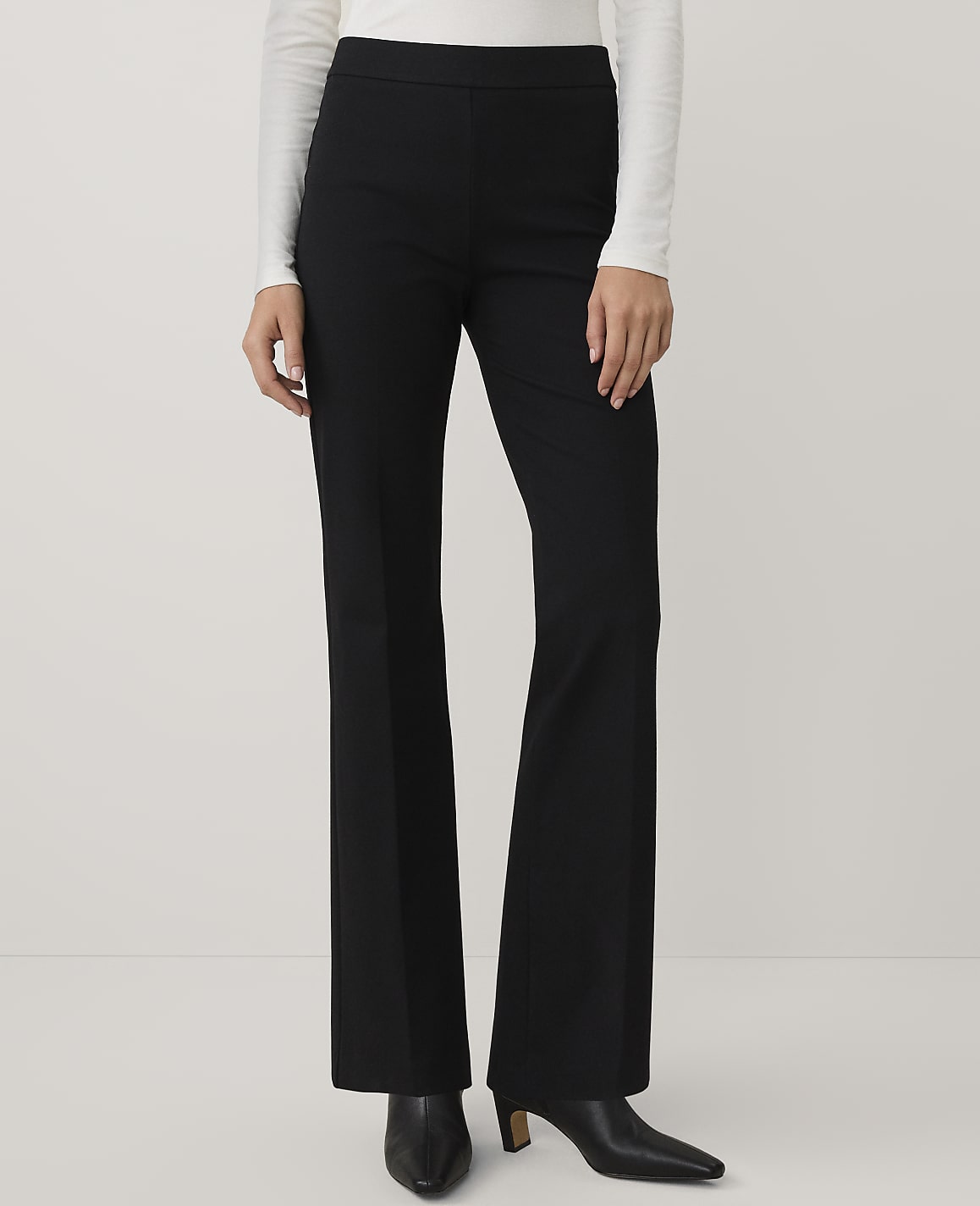 A person wearing a white long-sleeved top and black wide-leg trousers stands against a plain white background.