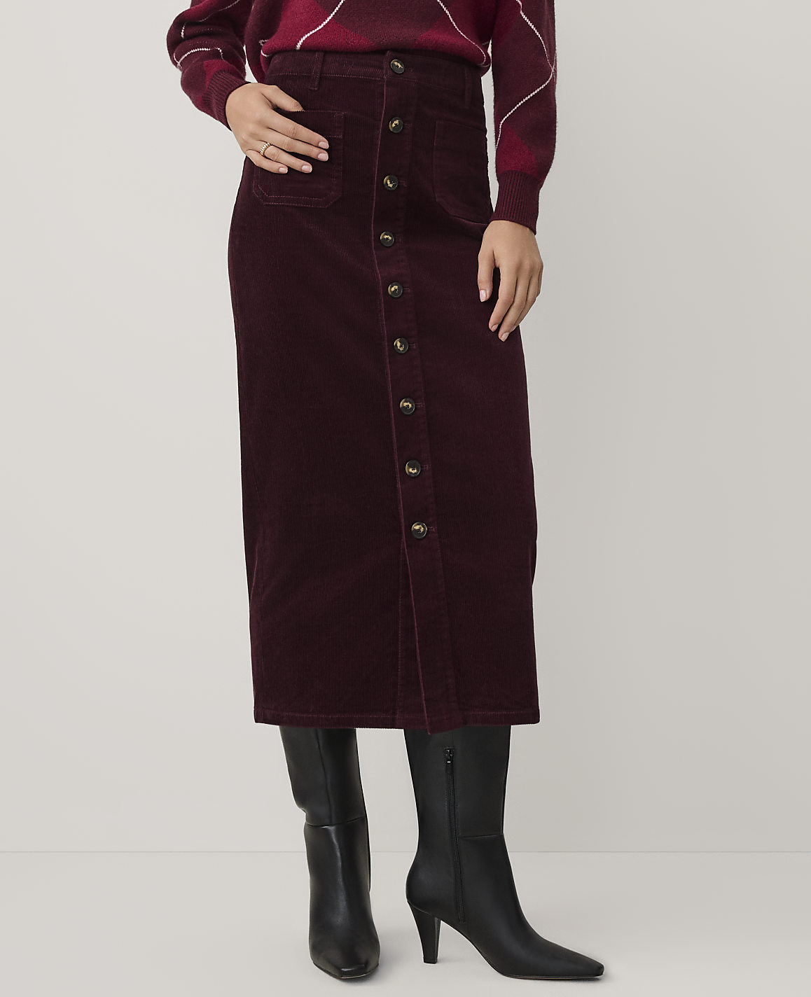 A person wears a burgundy corduroy button-down skirt and black boots against a plain white background.