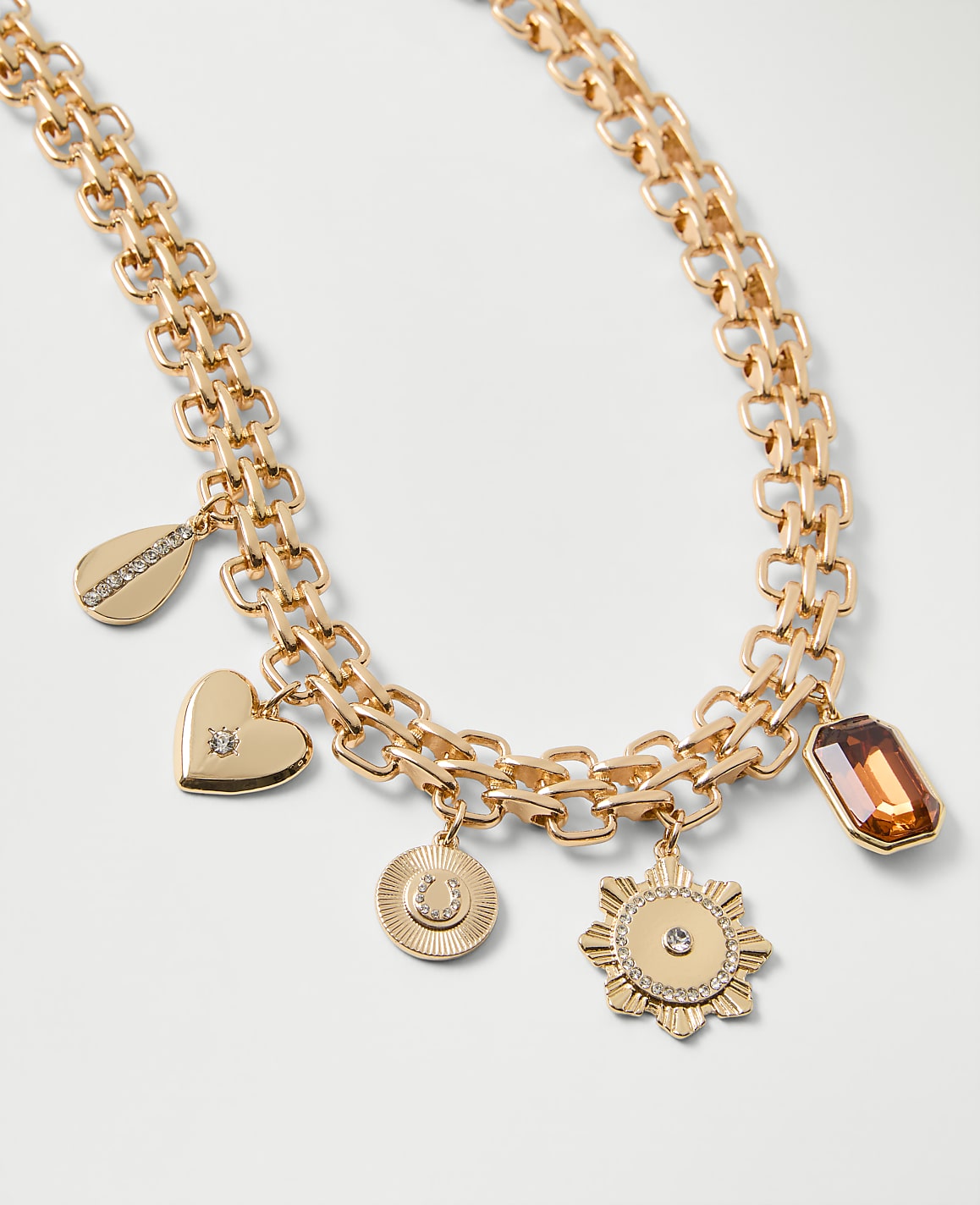 A gold chain necklace with various charms and a gemstone sits against a plain white background.
