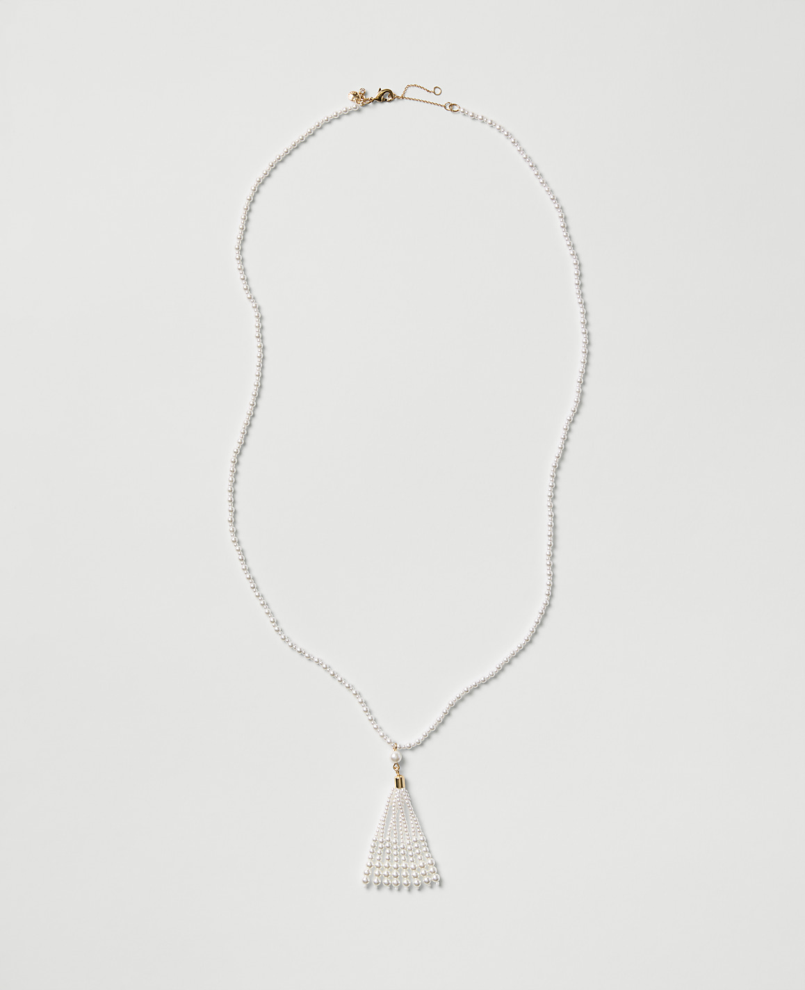 A white pearl necklace with a tassel pendant rests on a plain light gray background.