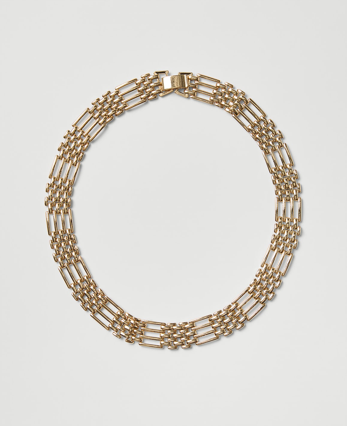 A gold chain necklace is arranged in a circle against a plain light gray background.