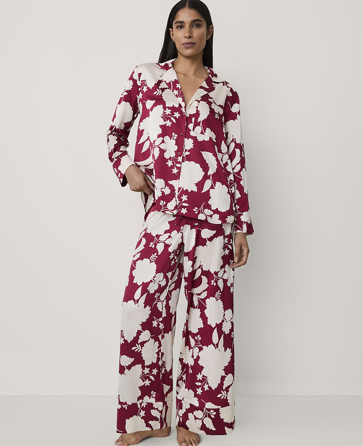A woman wearing red and white floral pajamas stands against a plain, light-colored background.