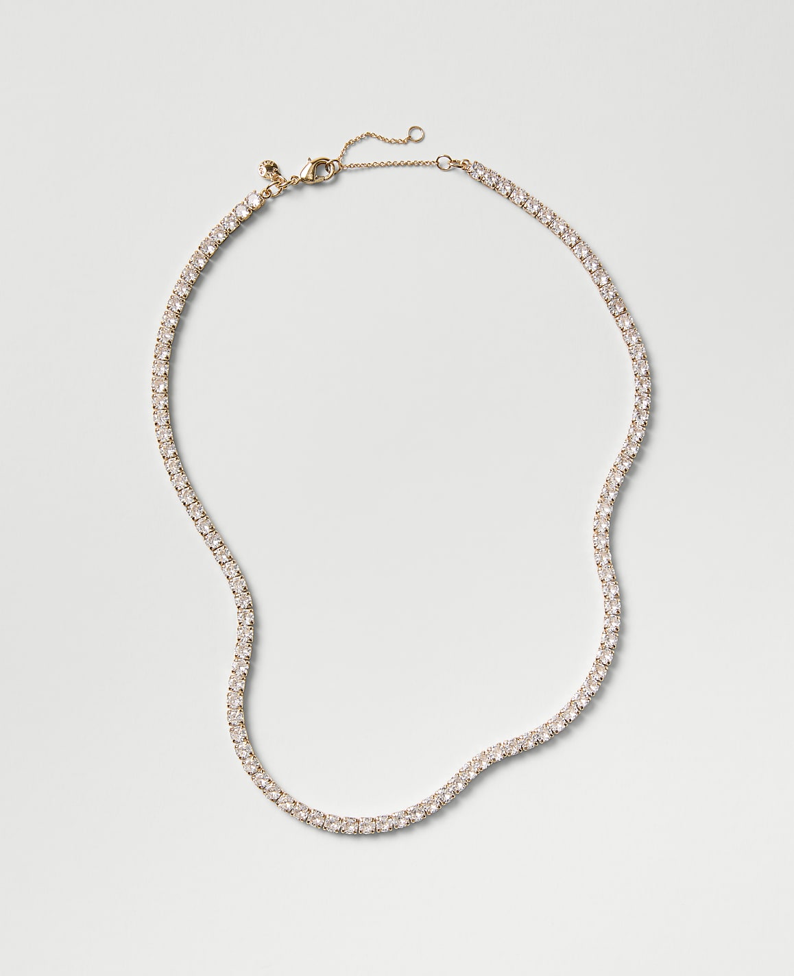 A sparkling tennis necklace with clear stones rests on a plain, light gray background.