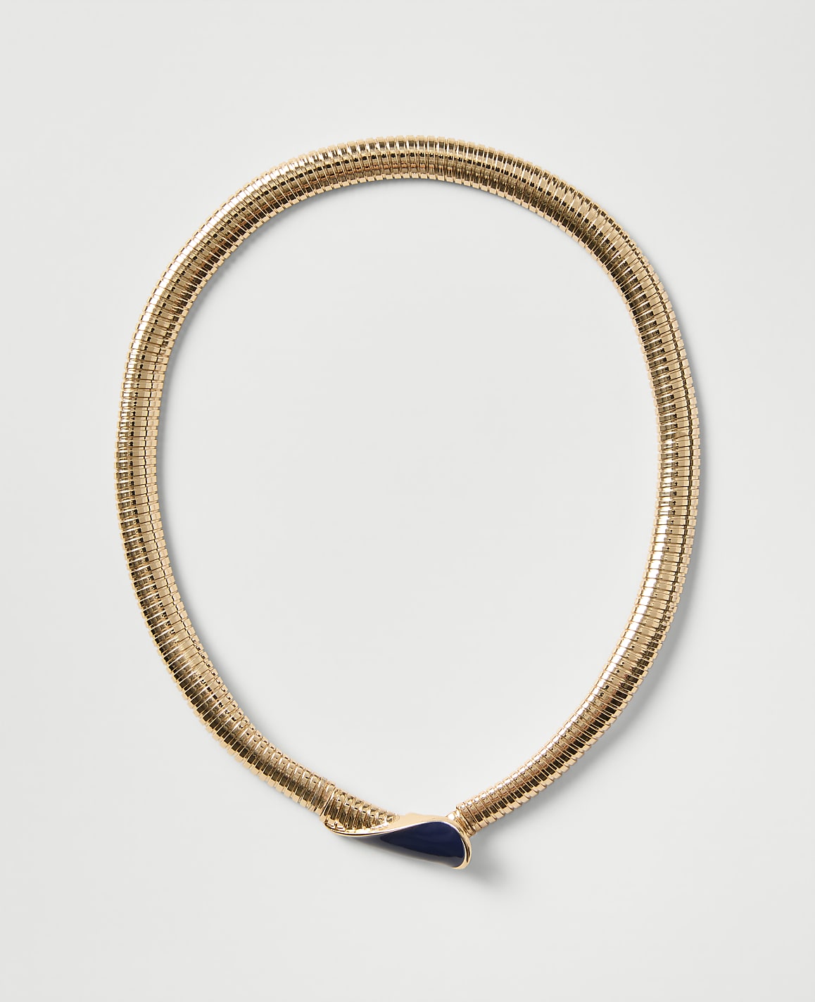 A gold ribbed necklace with a dark blue teardrop-shaped pendant rests on a plain light gray background.