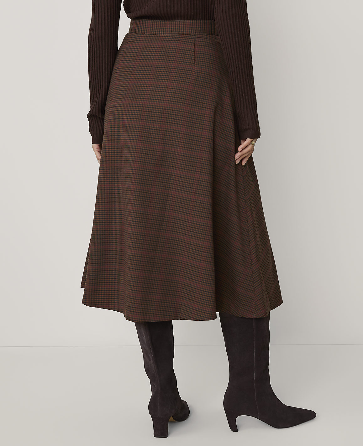 A person wears a brown ribbed top, a brown plaid A-line skirt, and dark brown boots against a plain light gray background.
