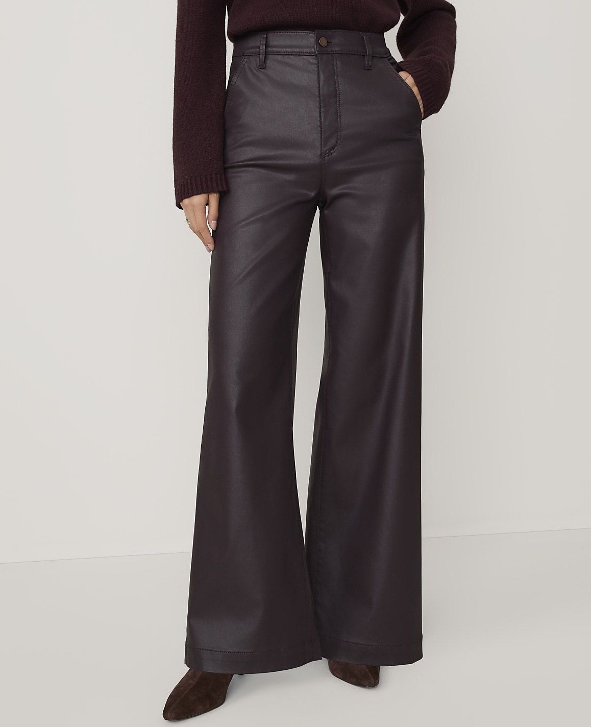 A person wears a dark burgundy sweater and wide-leg faux leather trousers against a plain white background.