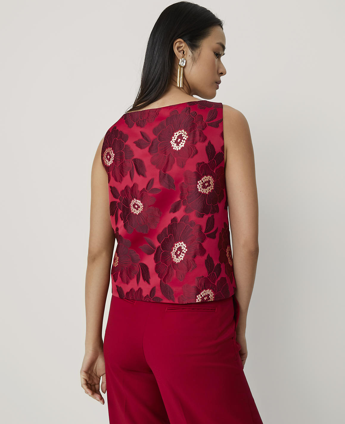 A woman wearing a red floral sleeveless top and matching red trousers stands against a plain, light-colored background.