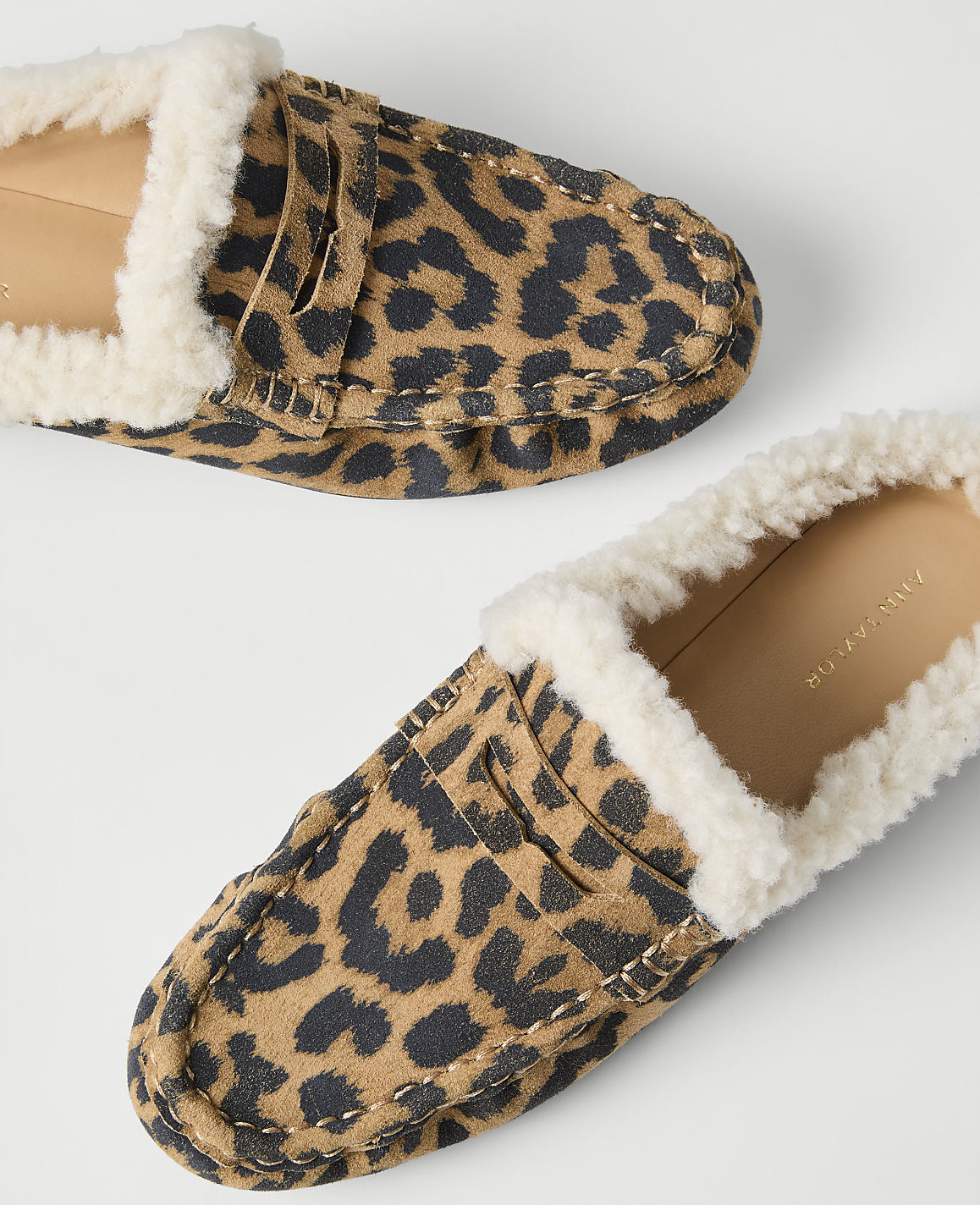 A pair of leopard-print loafers with white faux-fur lining rests on a plain white background.