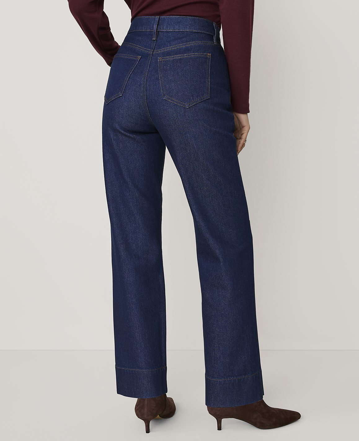 A person wearing a burgundy top and dark blue wide-leg jeans stands against a plain, light-colored background.