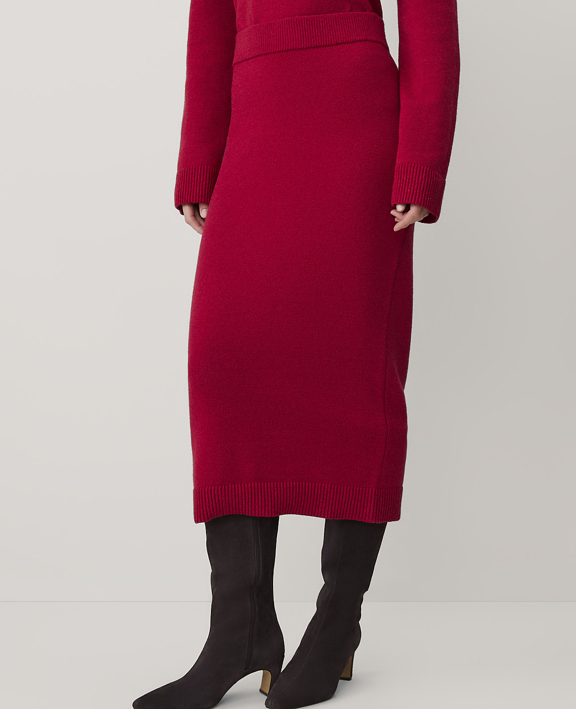 A person wearing a red knit skirt and black boots stands against a plain, light-colored background.