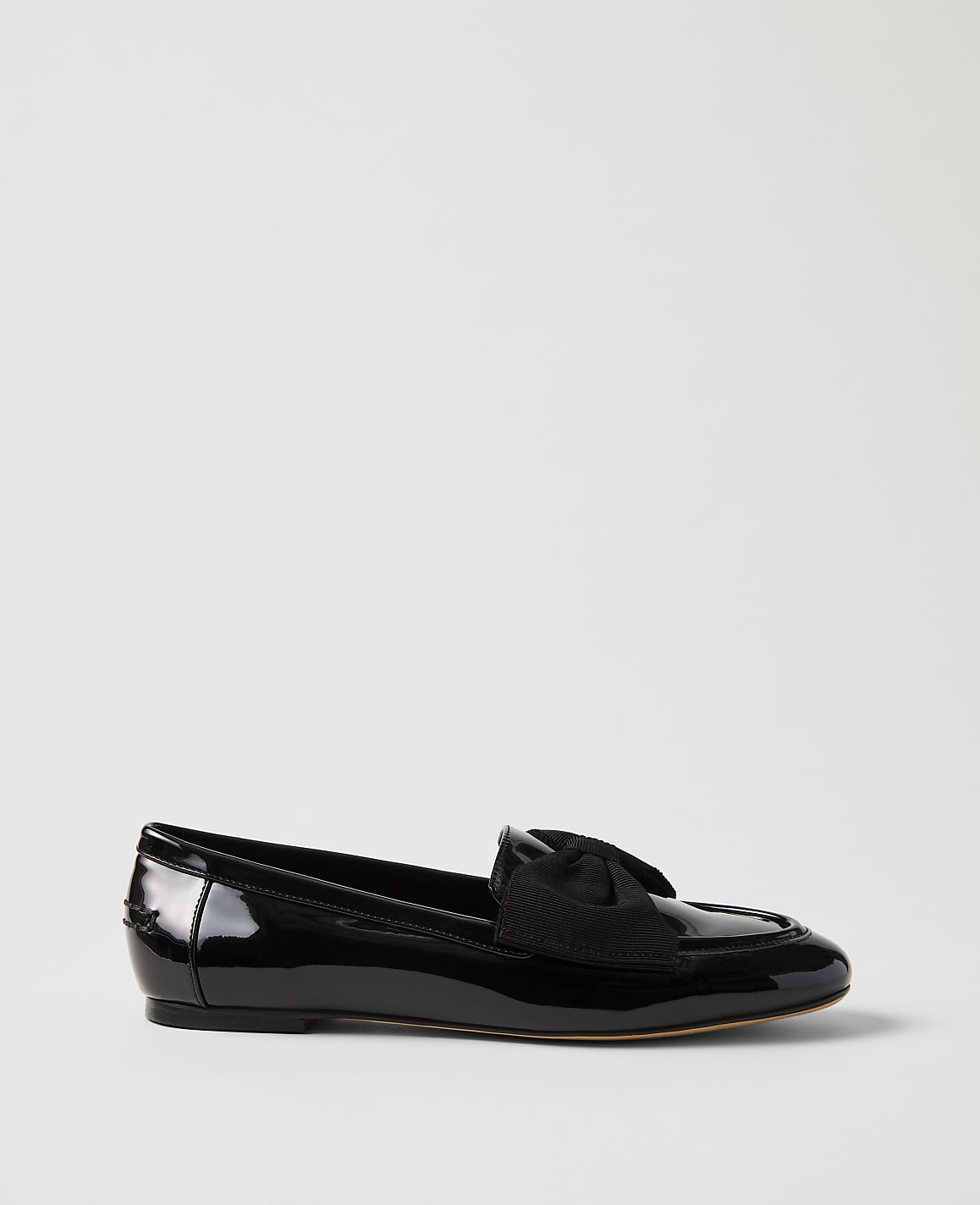 A single black patent leather loafer with a bow detail sits against a plain, light grey background.