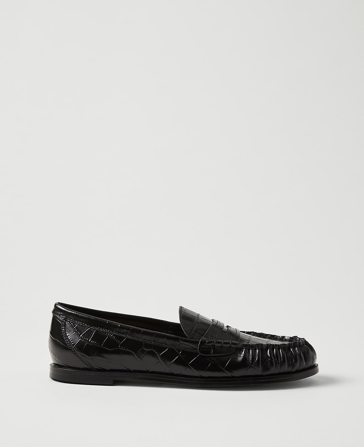 A single black crocodile-embossed leather loafer sits in the foreground against a plain, light grey background.