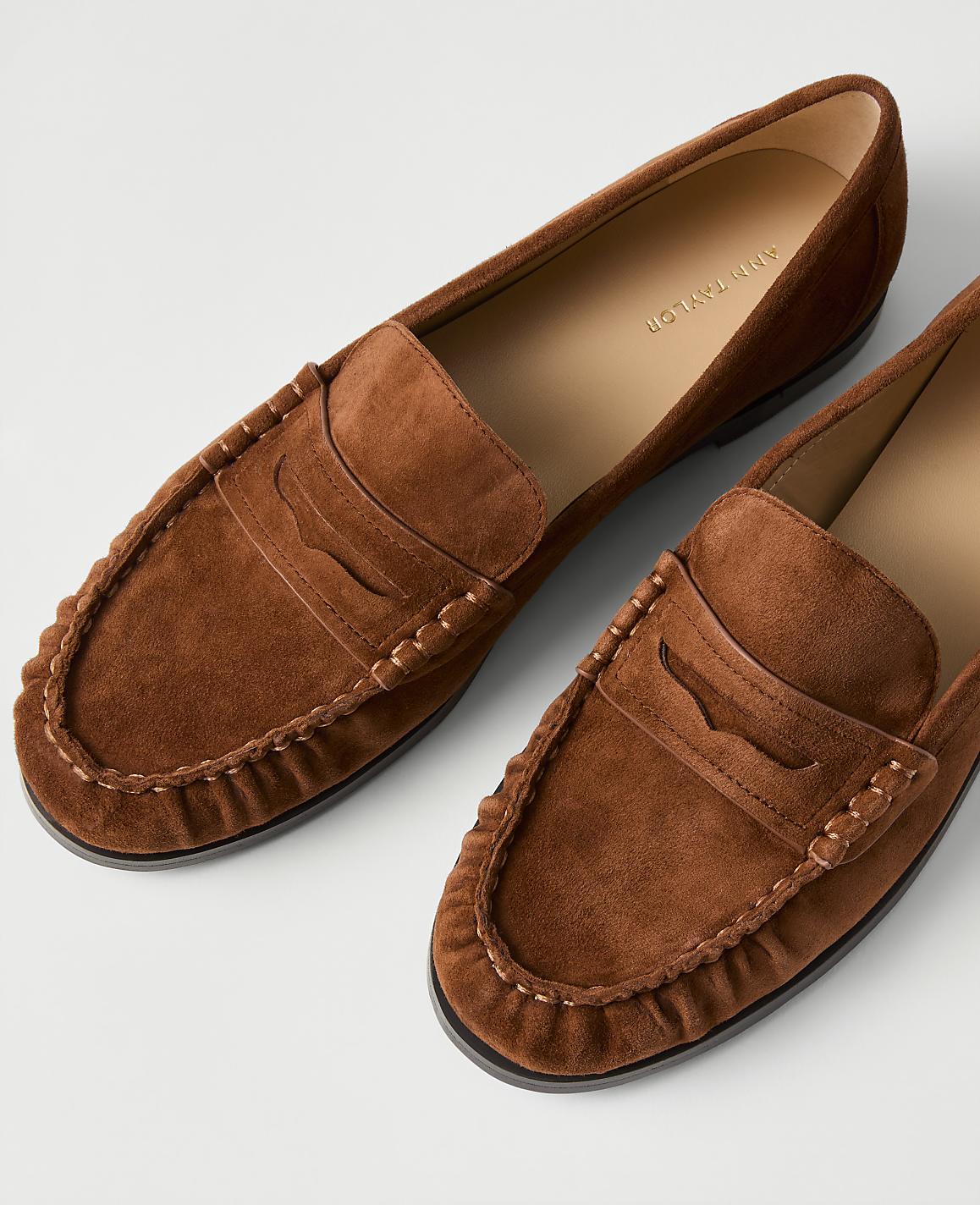A pair of brown suede loafers rests on a plain white background.