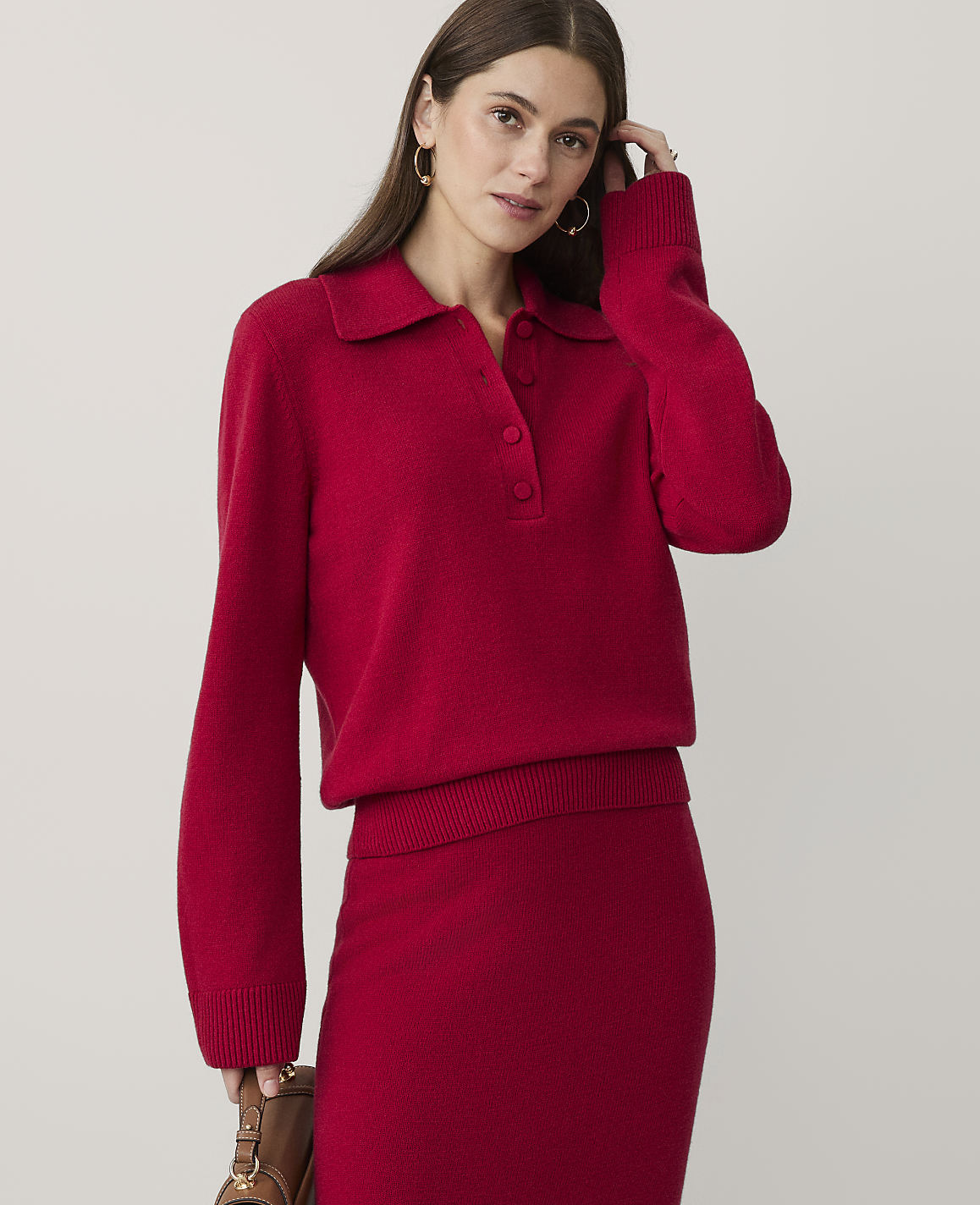A woman wearing a red knit sweater and matching skirt stands against a plain, light-colored background.