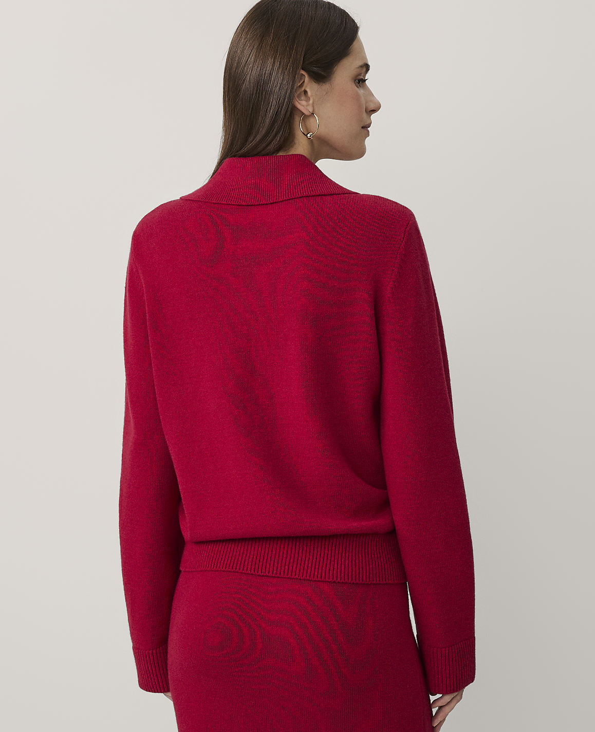 A woman wearing a red knit sweater and matching skirt stands against a plain, light-colored background.