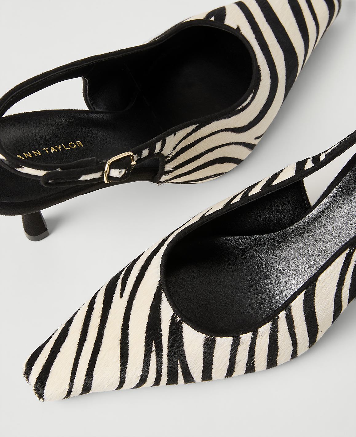 Two zebra-print pointed-toe pumps with black straps are positioned diagonally against a plain white background.
