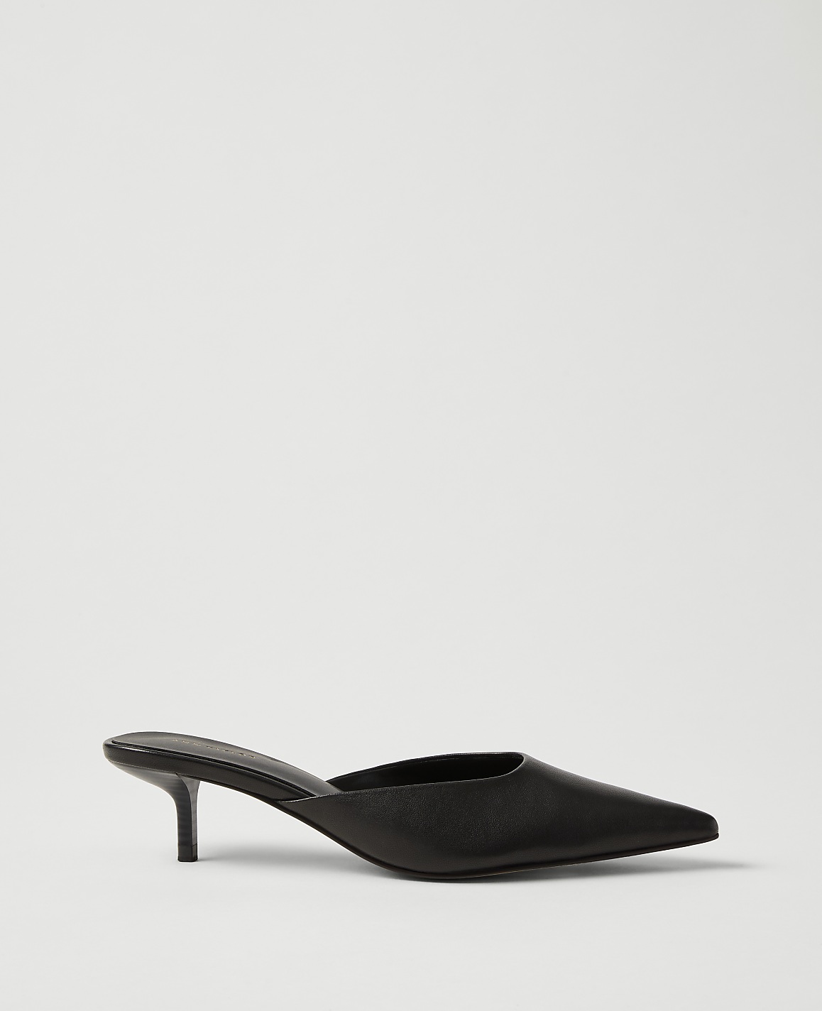 A single black pointed-toe kitten heel mule sits in the foreground against a plain, light gray background.